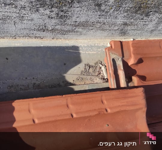 רעפים חומים על גג עם קיר בטון אפור